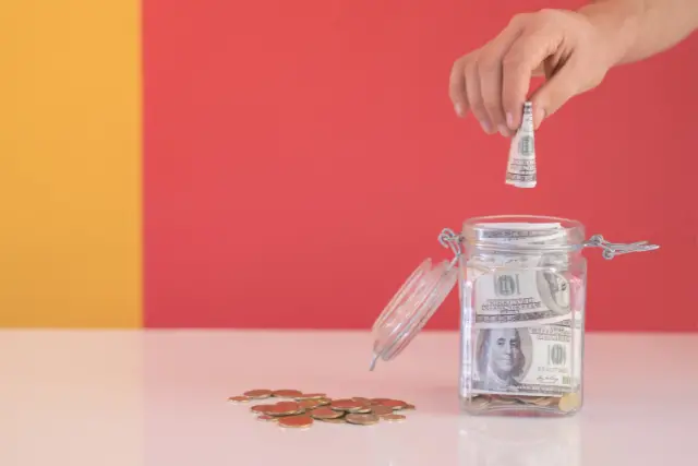 Someone dropping money into a jar representing saving up an emergency fund.
