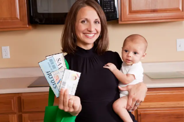 Mom holding coupons with one hand and holding a child in her other arm