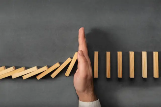 Person stopping dominos from continueing by putting thier hand in in front of the falling dominos, representing putting boundaries in ones life