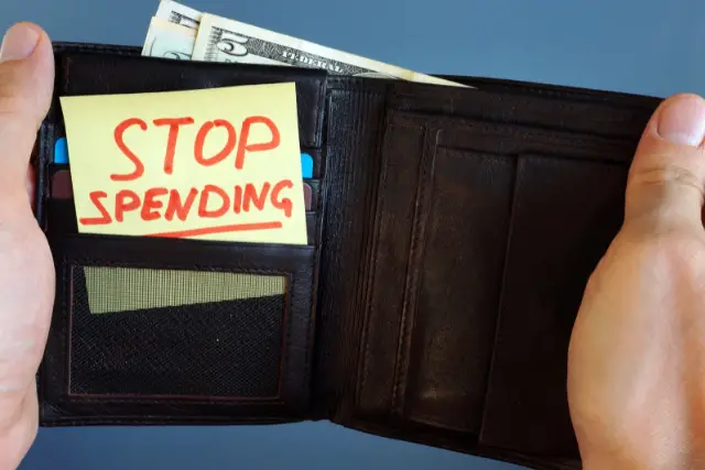 Opened wallet that says "STOP SPENDING" on a post it note inside