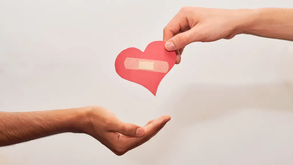 One person giving another person a paper heart with a bandaid on it.